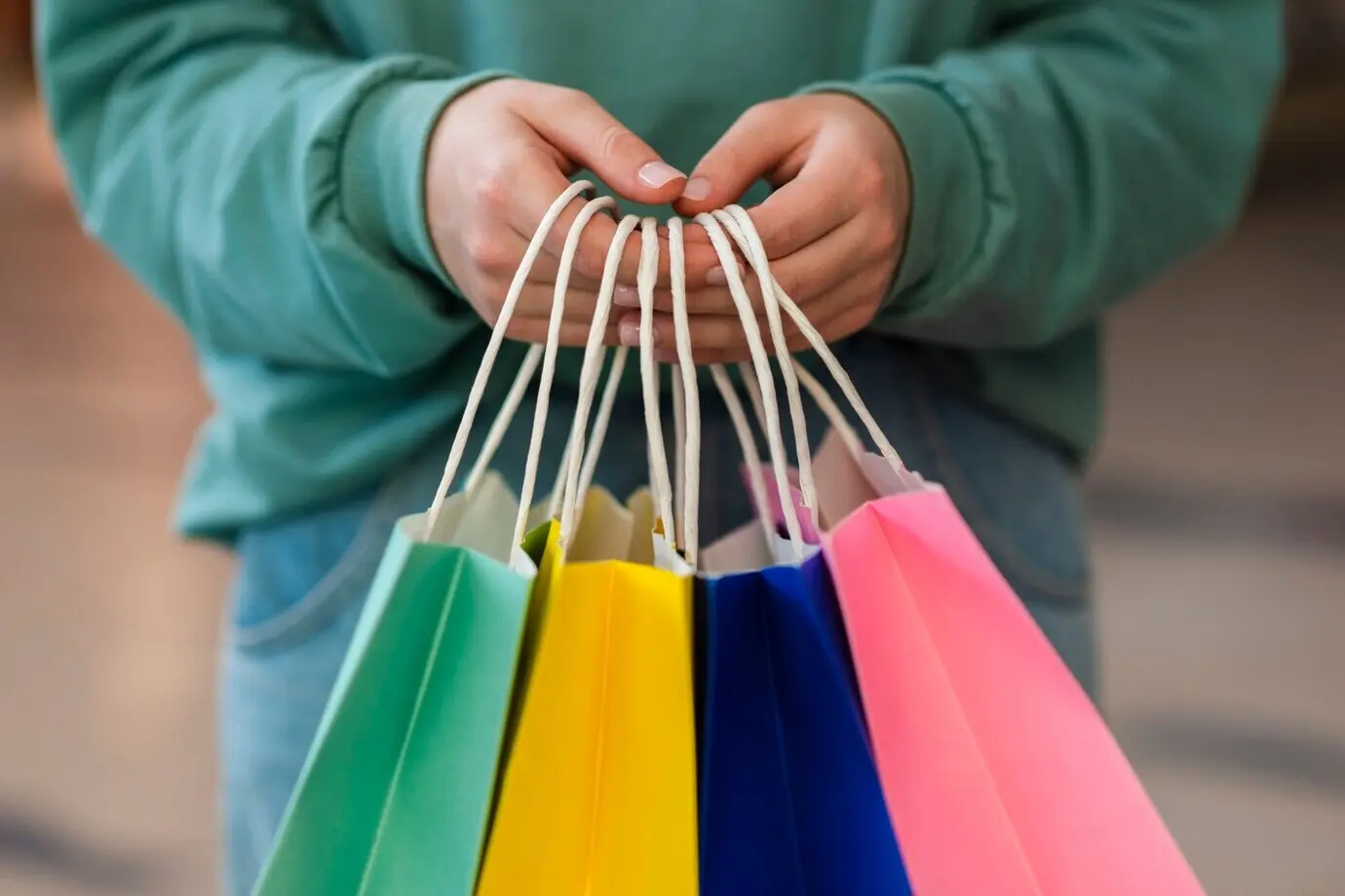 Vista frontal de manos que sostienen bolsas de papel de colores.