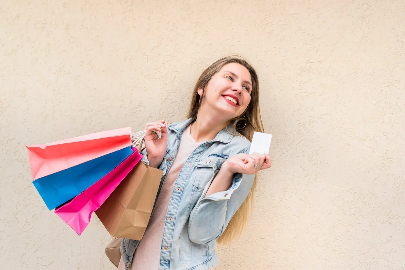 Mujer feliz de pie junto a una pared, con bolsas de compras y tarjeta de crédito